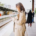 駅のホームでスマートフォンを見る一人旅の女性
